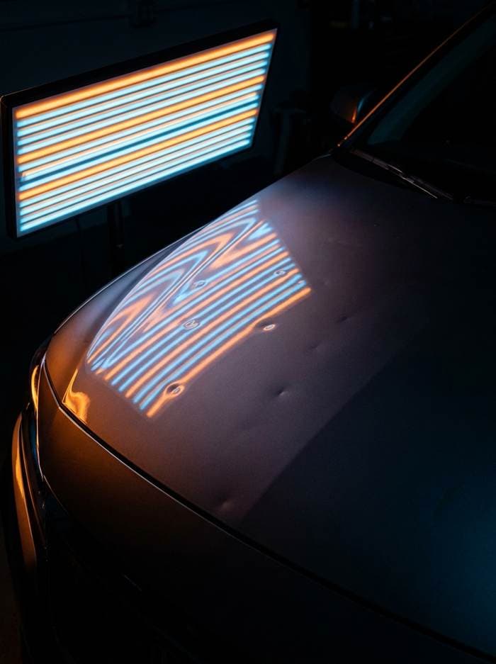 Car hood under a PDR reflector light, the lines revealing hail dents